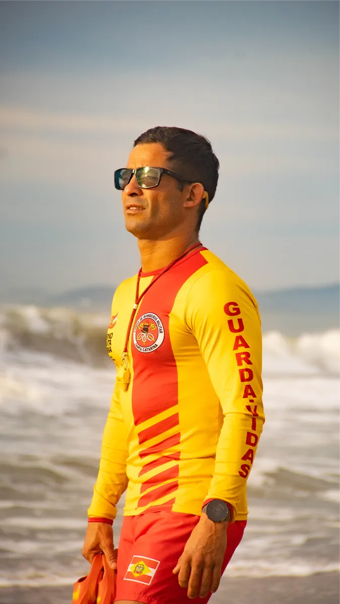 Hermes com o uniforme amarelo e vermelho de guarda-vidas, na beira do mar